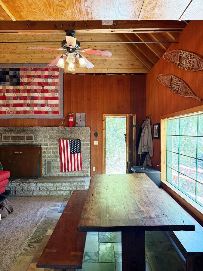 Long plank dining table with benches beside the stone wood fireplace, flag quilt and snowshoes on the wall