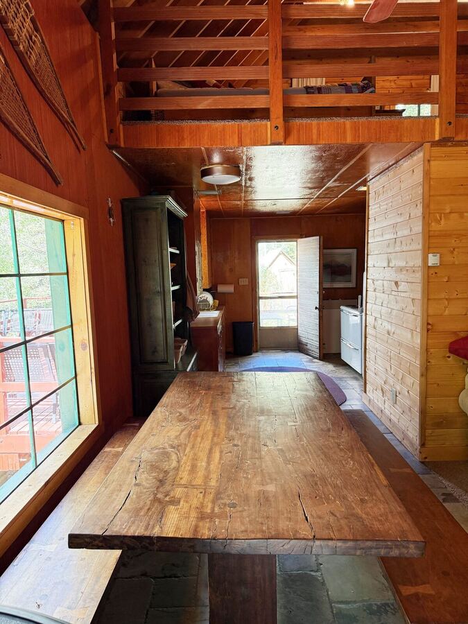 View along the dining table toward the front door, with the bunk loft railing overhead