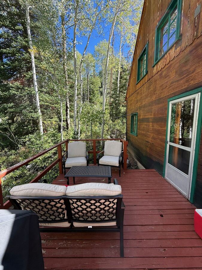 Cushioned chairs and a low table on the side deck, aspens beyond the railing