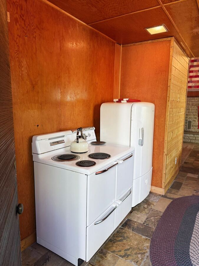 Original 1940s white stove and rounded refrigerator in the wood-paneled kitchen
